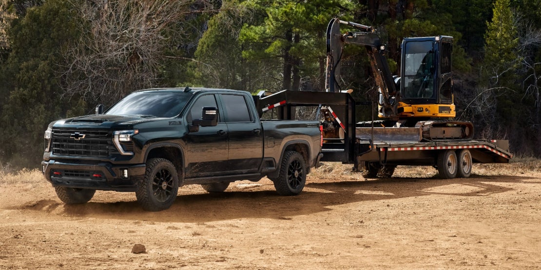 A dark green Chevy Silverado 2500 towing a construction vehicle.