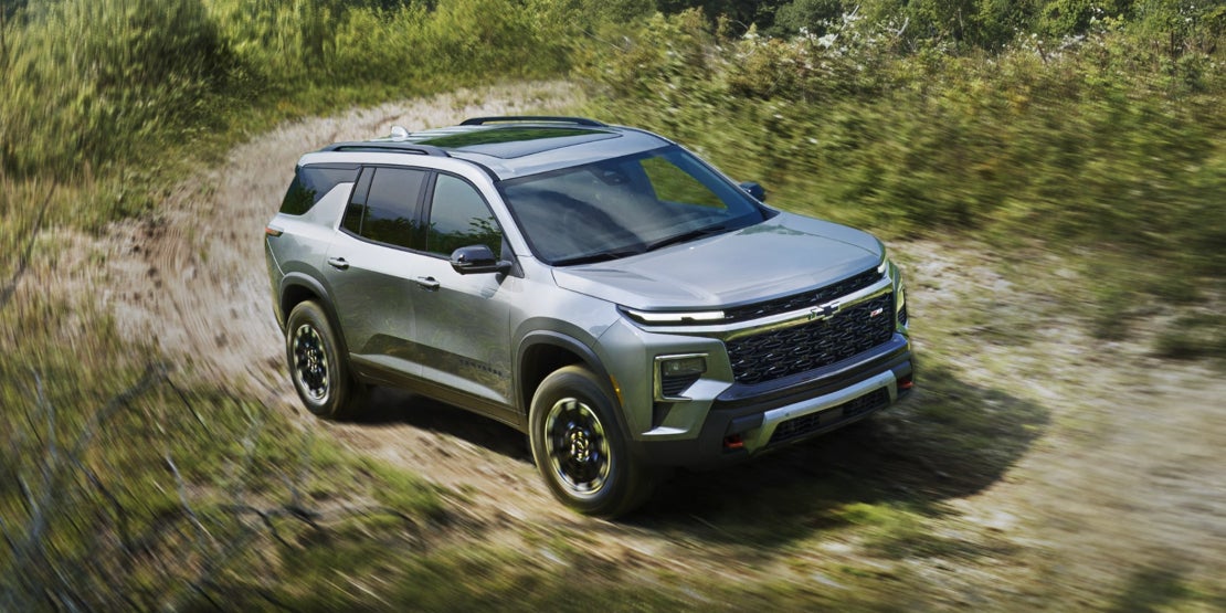 A gray Chevrolet Traverse driving over a dirt road through a field.