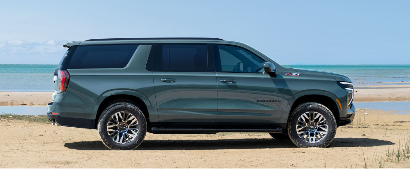 A teal Chevrolet Suburban in profile on a beach.