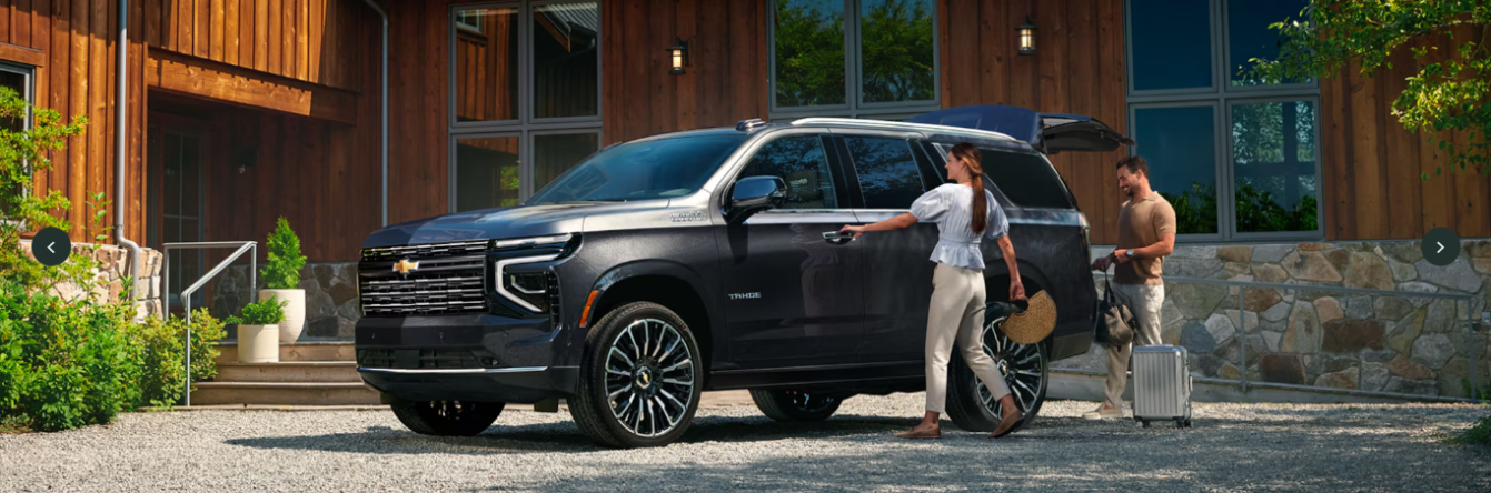 A couple loading up a black Chevrolet Tahoe in front of a large building.