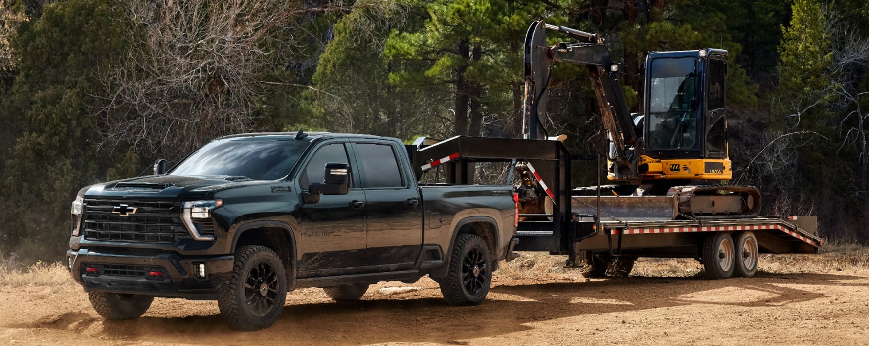 A dark green Chevy Silverado 2500 towing a construction vehicle.