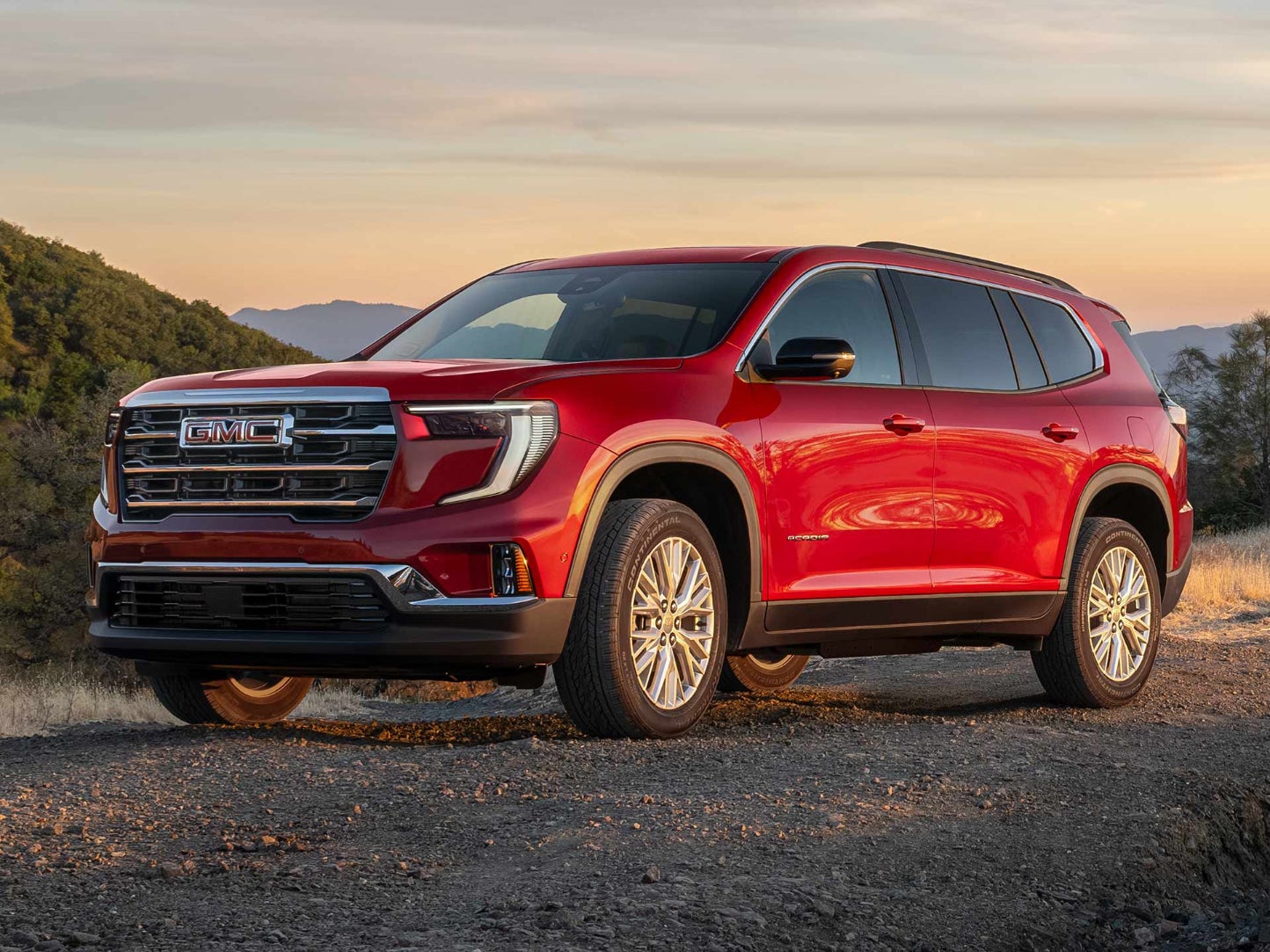 A red GMC Acadia driving on a dirt road.