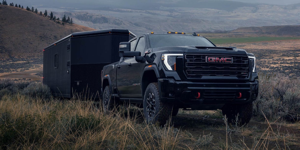 A black GMC Sierra HD towing a black trailer off-road through some grasslands.