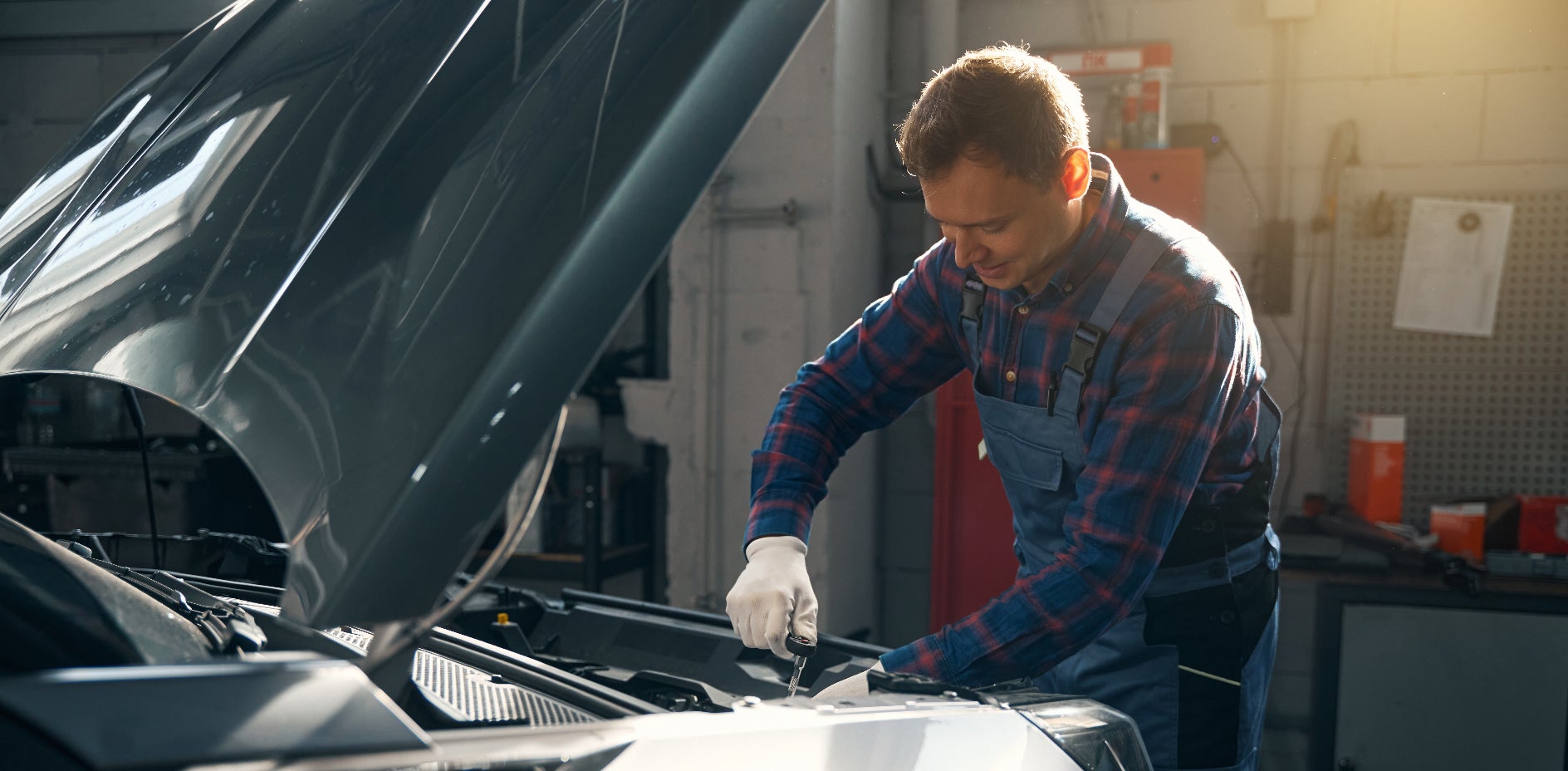 An engineer repairing a vehicle with its hood up.